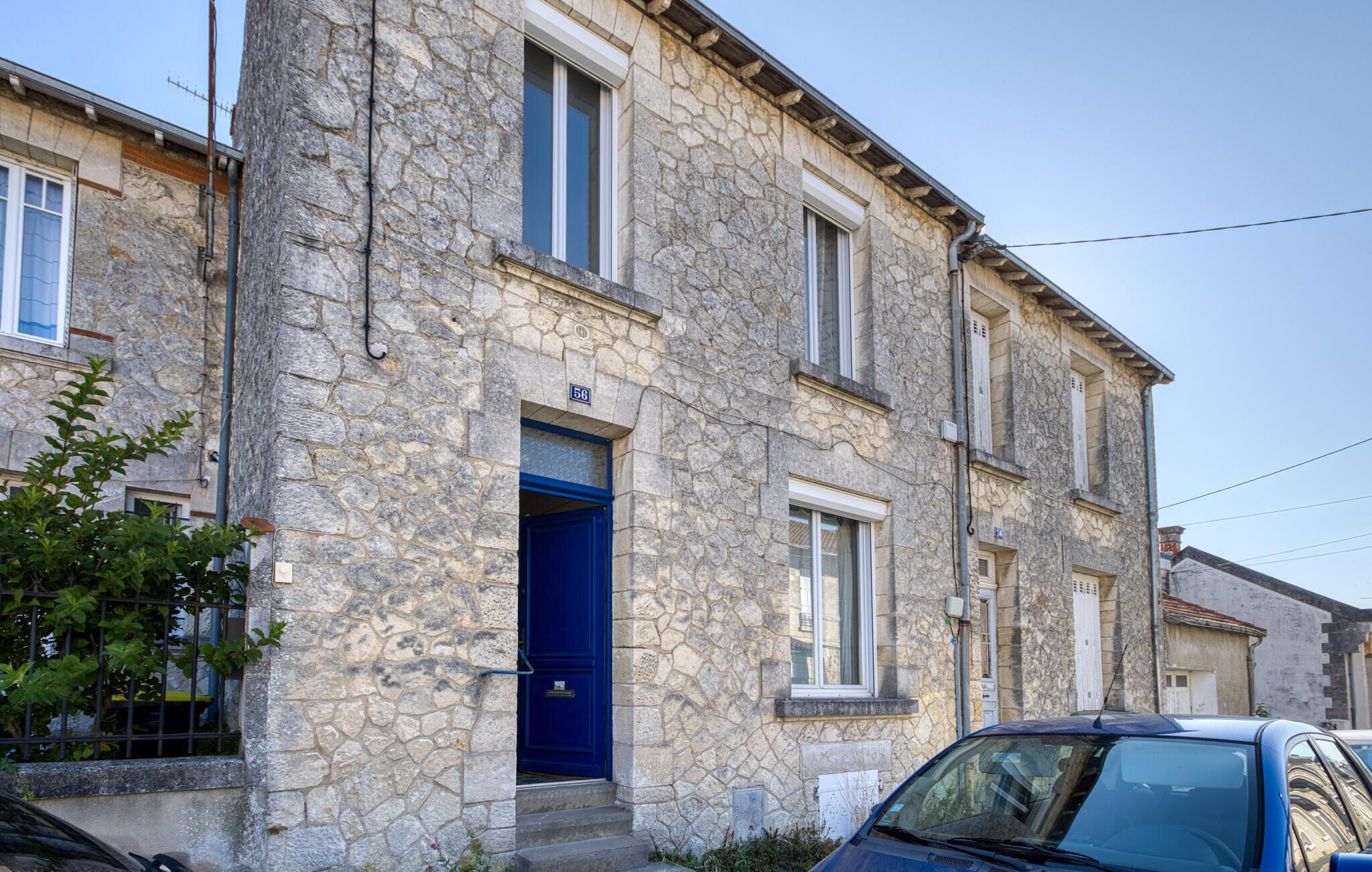 A stone building with a blue door, numbered 58, and a car parked in front.