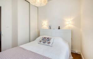 A neatly arranged bedroom with a bed, bedside lamps, and a wall-mounted telephone. - Charmante Maison Proche Plage (La Rochelle)
