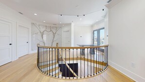 Un interior espaiós i modern amb una escala de fusta corba, parets blanques i un disseny de paret semblant a marbre.