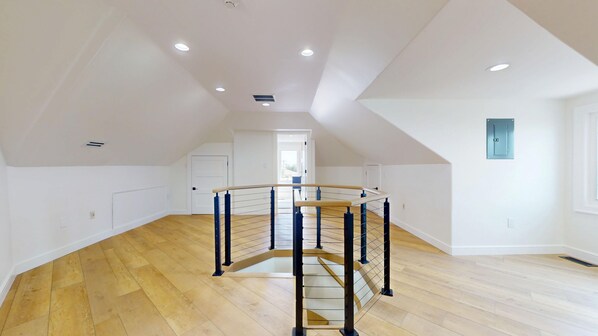 A spacious attic room with a wooden floor, a central staircase, and a skylight.