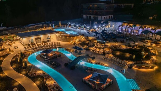 A resort with a winding pool, outdoor seating areas, and a building with illuminated signage. - Sleeps 21 | Indoor Pool | Resort Waterpark | Views (Sevierville)