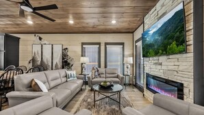 A modern living room with a stone fireplace, a large flat-screen TV, and a ceiling fan. - Sleeps 21 | Indoor Pool | Resort Waterpark | Views (Sevierville)