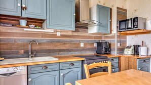 A compact kitchen with blue cabinets, a stainless steel sink, a microwave, a toaster, and a wooden dining table.