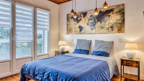 A bedroom with a large bed, two nightstands, a world map artwork, and a wooden ceiling.