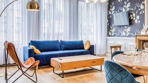 A modern living room with a blue sofa, wooden coffee table, and a dining area with a round table.
