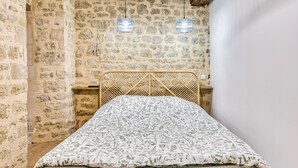 A room with a stone wall, a bed with a patterned bedspread, and two hanging light fixtures.