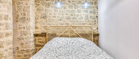 Una habitación con pared de piedra, una cama con colcha estampada y dos lámparas colgantes.