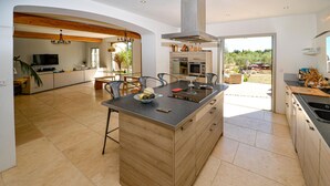 A spacious kitchen with a central island, wooden cabinetry, and a large window offering a view of the outdoors. - Amazing home in Venelles (Venelles)
