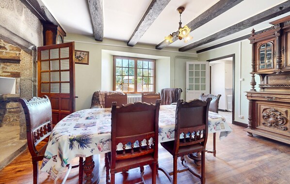 Uma sala de jantar com uma mesa e cadeiras de madeira, um candelabro e uma janela grande.