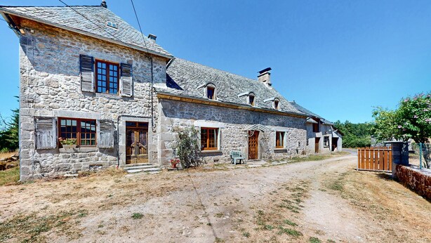 A stone house with a dirt driveway, wooden doors, and a small porch area.