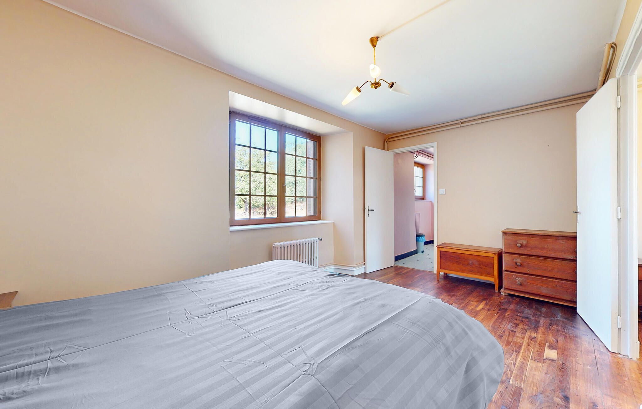 A bedroom with a large bed, a wooden dresser, a radiator, and a window.