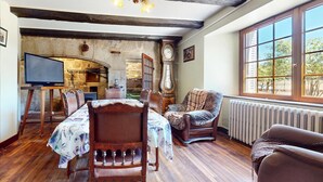 A rustic dining area with a wooden table and chairs, a television, and a stone wall.