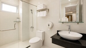 A modern bathroom with a glass shower enclosure, a white toilet, a black countertop with a white sink, and a glass shelf with toiletries. - Thu Ha Airport Hotel (Ho Chi Minh City)