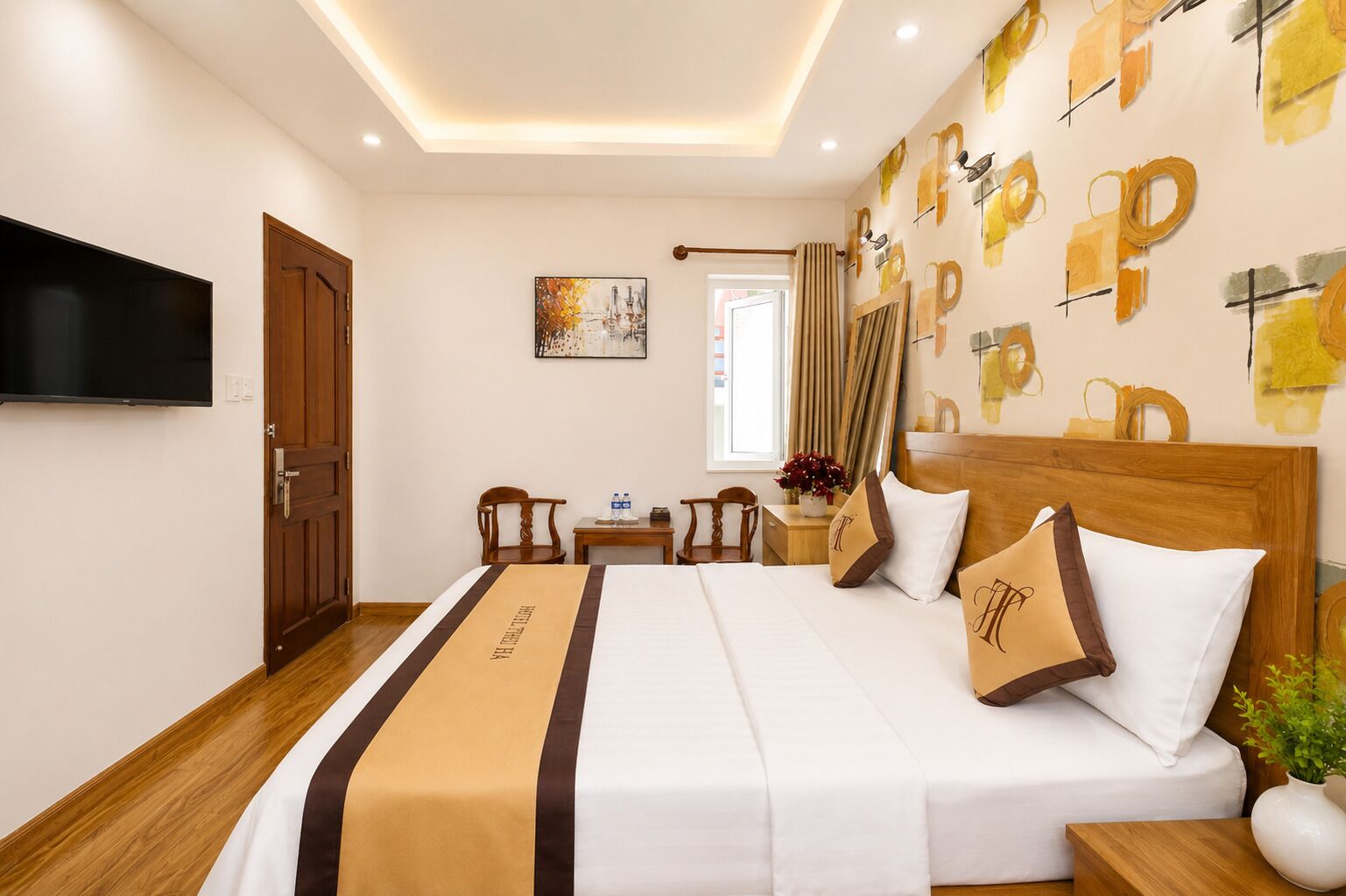 A hotel room with a bed, a TV, a wooden door, a painting, and a window with curtains.
