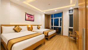 A hotel room with two beds, a desk, a chair, a window, and a picture on the wall. - Thu Ha Airport Hotel (Ho Chi Minh City)