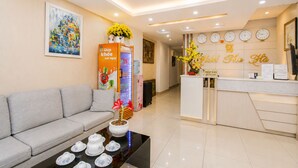 A hotel reception area with a sofa, a coffee table with teacups, a refrigerator, and a reception desk. - Thu Ha Airport Hotel (Ho Chi Minh City)