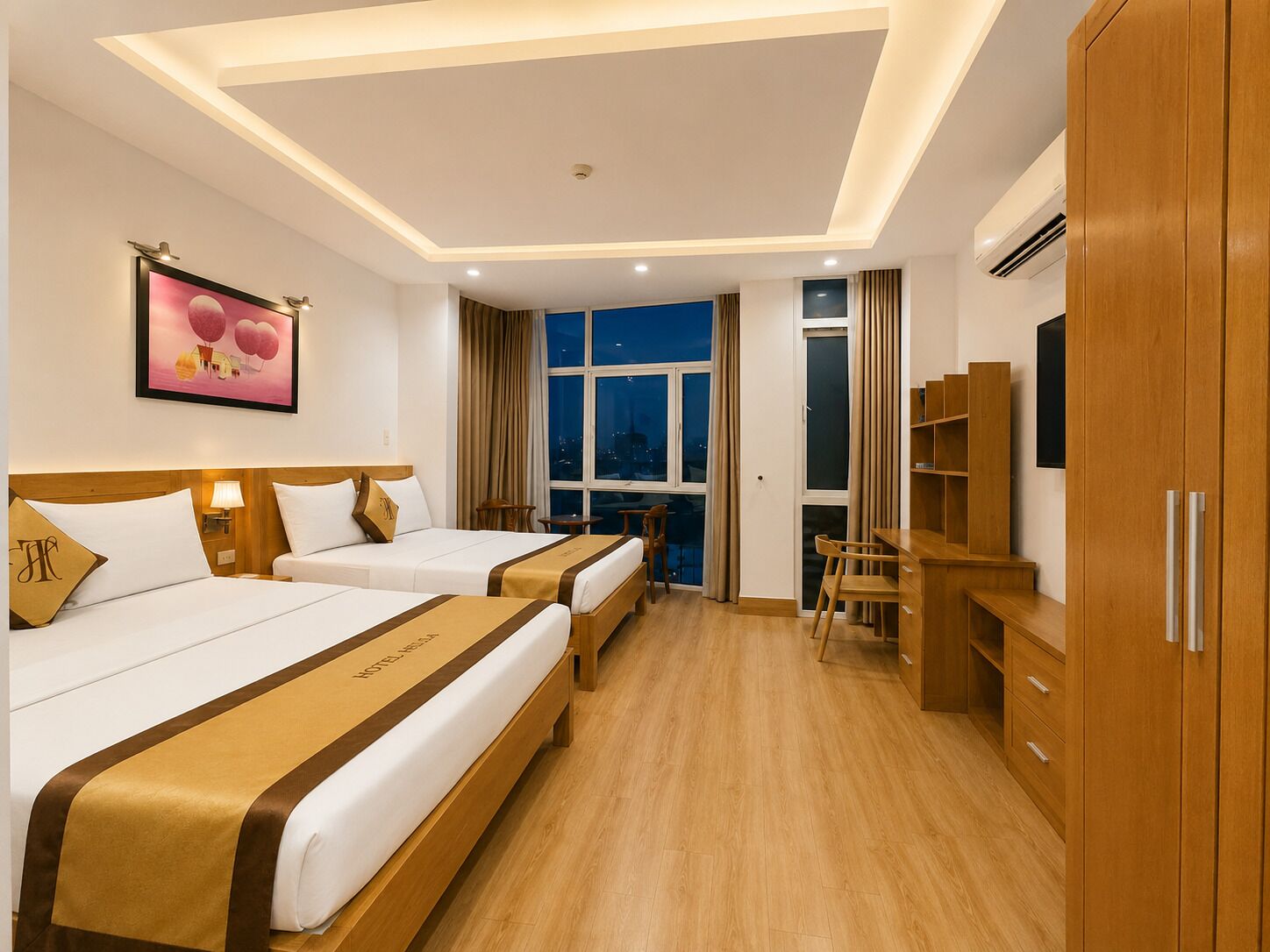 Habitación de hotel con dos camas, un escritorio, una silla, un televisor y un ventanal amplio.