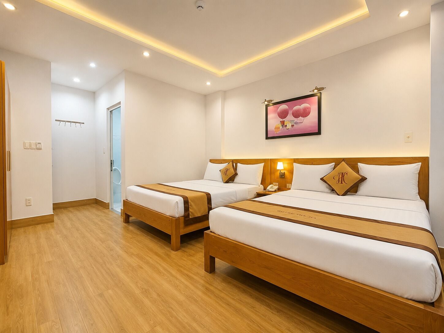 A hotel room with two beds, wooden headboards, a bedside table with a lamp, and a wall-mounted artwork.