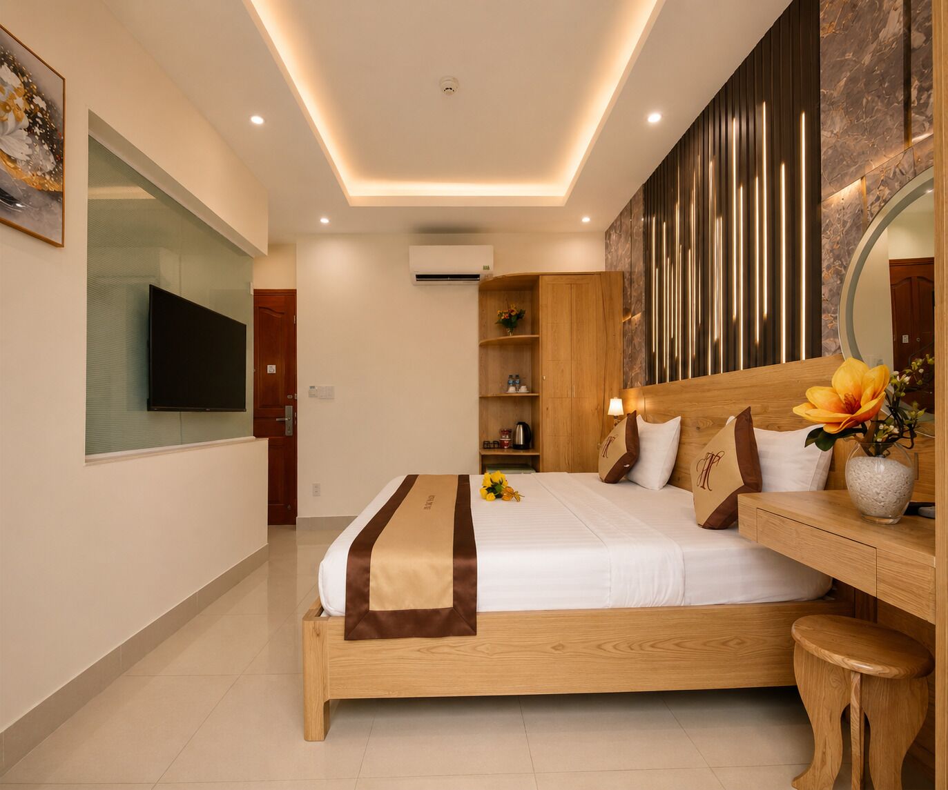 A modern hotel room with a wooden bed, a flat-screen TV, a vanity with a mirror, and a decorative wall panel.
