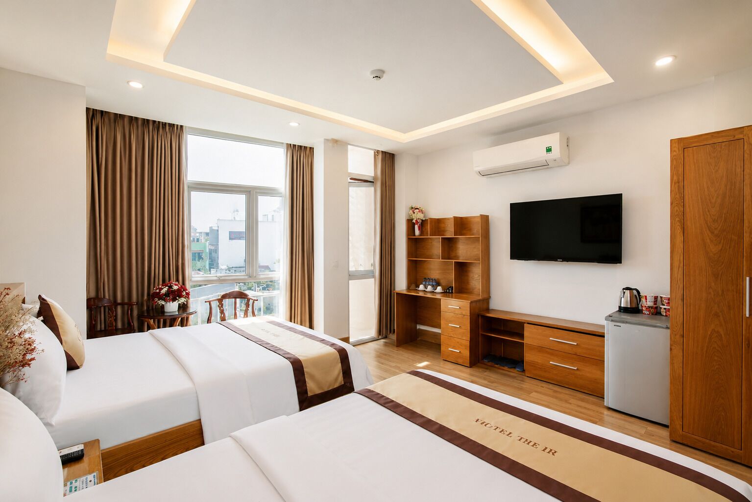 Habitación de hotel con dos camas, televisión, escritorio y kitchenette.