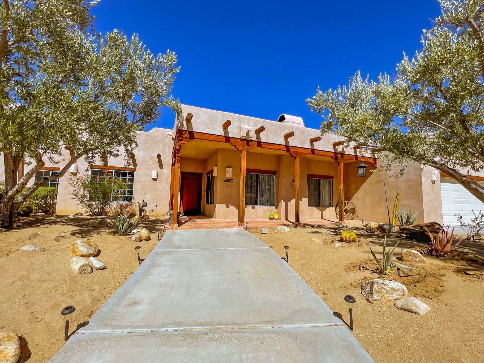 A desert-style building with a concrete pathway leading to the entrance, surrounded by cacti and rocks.
