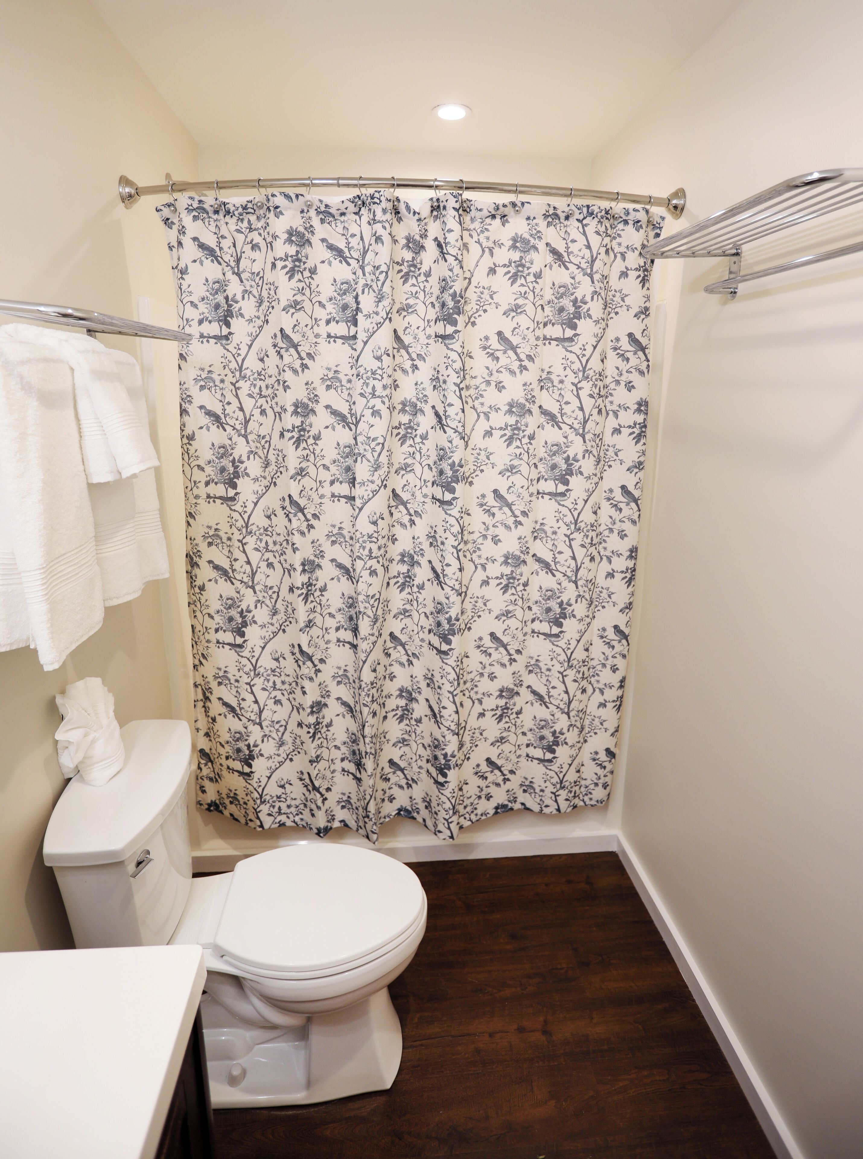 A bathroom with a toilet, a shower curtain with a floral pattern, and a towel rack with towels.