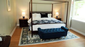 A four-poster bed with a dark headboard, two bedside tables with lamps, a dark blue upholstered bench, and a patterned rug.