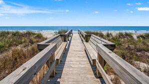 Un paseo marítimo de madera que conduce a una playa con cielos despejados.