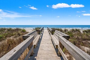 Une promenade en bois menant à une plage, avec un ciel dégagé.