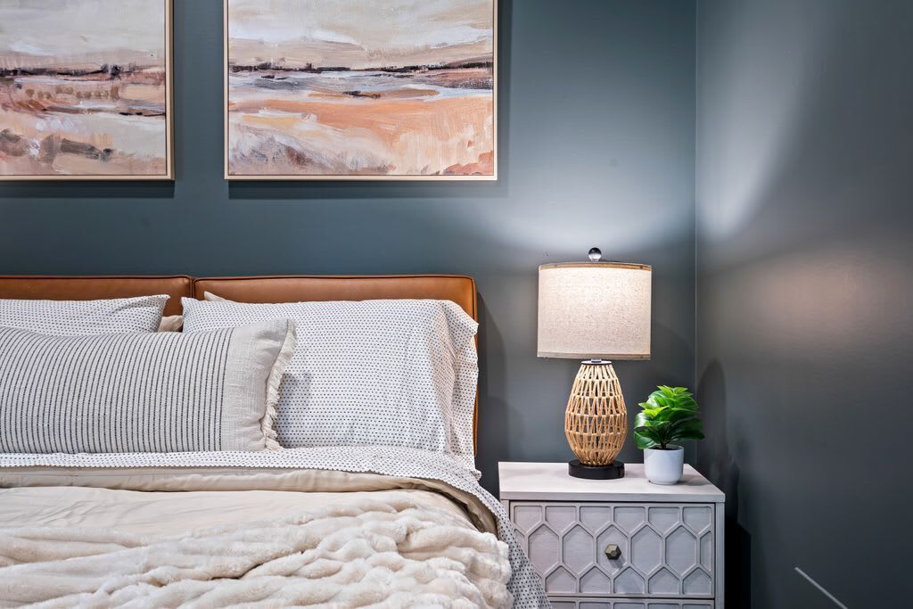 A bedroom with a bed, a nightstand, a lamp, and two wall-mounted paintings.