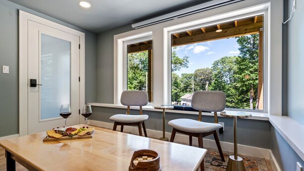 A dining area with a wooden table, two chairs, and a window with a view of trees. - Cozy 1 BR ADU | Private Access | Projector Theater (Windham)