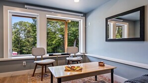 A modern living room with a large window, two chairs, a table with snacks, and a mirror on the wall. - Cozy 1 BR ADU | Private Access | Projector Theater (Windham)