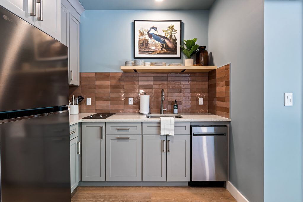 A modern kitchen with grey cabinets, a stainless steel refrigerator, and a sink.