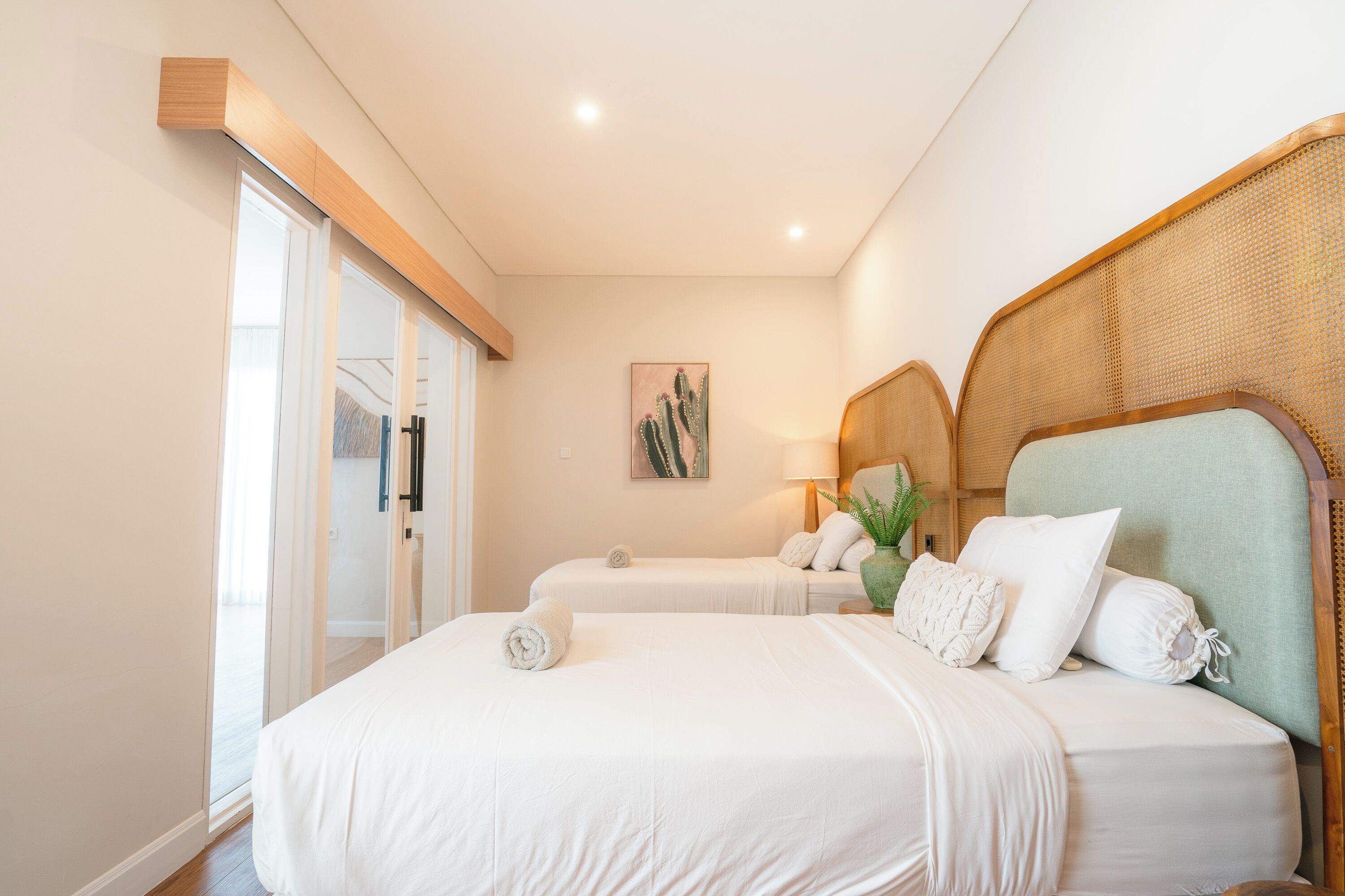 Un cuarto de hotel con una cama grande, una cama más pequeña, un ventanal con vista y una obra de arte con cactus en la pared.