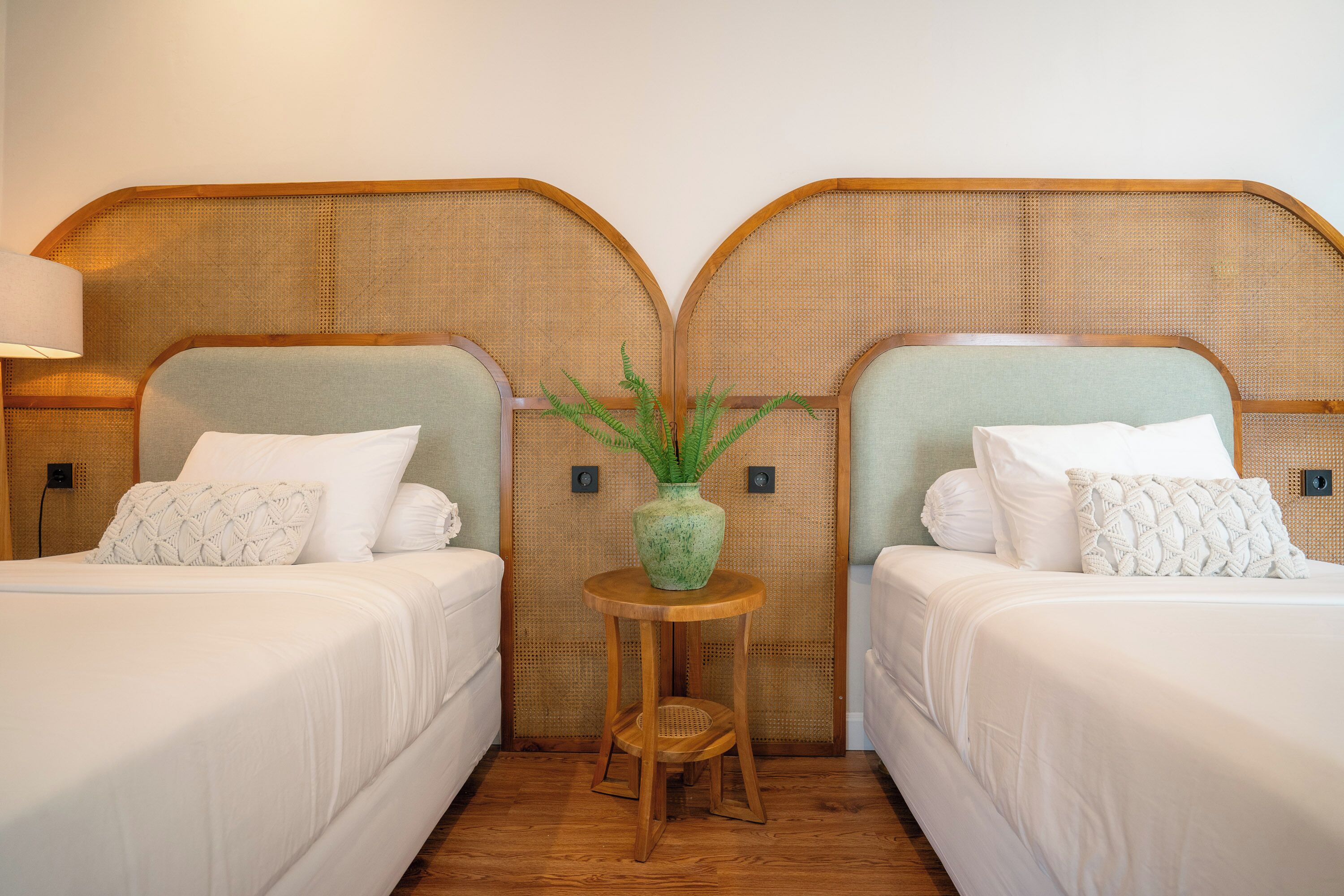 Een hotelkamer met twee bedden, een klein houten tafeltje met een vaas en een geweven hoofdbord.