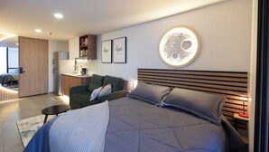 Ein modernes Schlafzimmer mit einem großen Bett, einer Couch, einem kleinen Tisch und einer Küchenzeile.