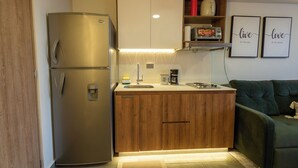 Eine kompakte Küche mit Edelstahlkühlschrank, Holzschränken, einem eingebauten Backofen und einer Kaffeemaschine.