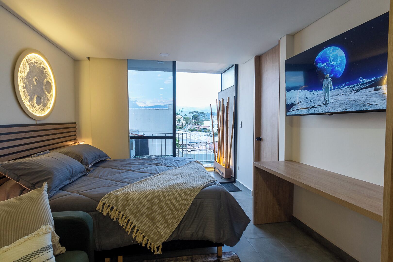 Un dormitorio moderno con una cama grande, vistas de la ciudad y una obra de arte mural con temática espacial.