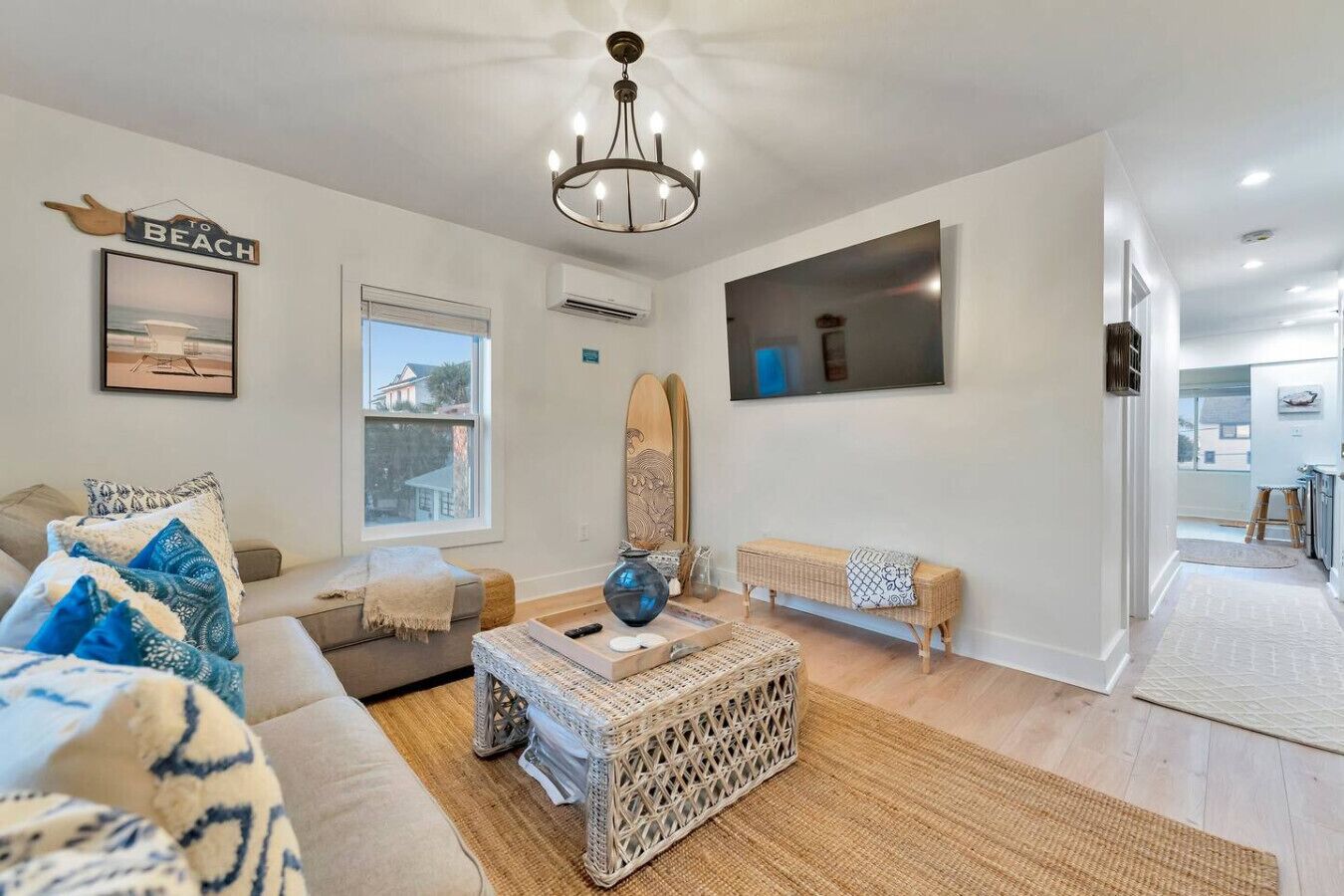 A modern living room with a sofa, a coffee table, a surfboard, and a beach-themed sign.