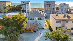 A beachfront property with a thatched-roof structure, a staircase leading to a balcony, and a view of the ocean. - Tiki House  - Sandy Toes Escape Walk to Beach (Treasure Island)