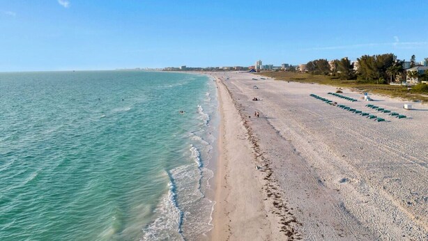 A wide beach with clear turquoise waters and a sandy shore.