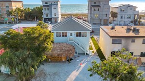 A beachfront property with a thatched-roof structure, a staircase leading to a balcony, and a view of the ocean.