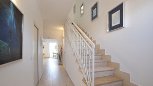 Un escalier avec des rampes blanches menant à l’étage supérieur, un couloir avec un plancher en bois et des œuvres d’art encadrées accrochées aux murs.