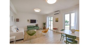 Un salon moderne avec un canapé, un meuble vert, un téléviseur et un coin repas avec des chaises.