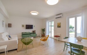 Una sala de estar moderna con un sofá, un armario verde, un televisor y un comedor con sillas.