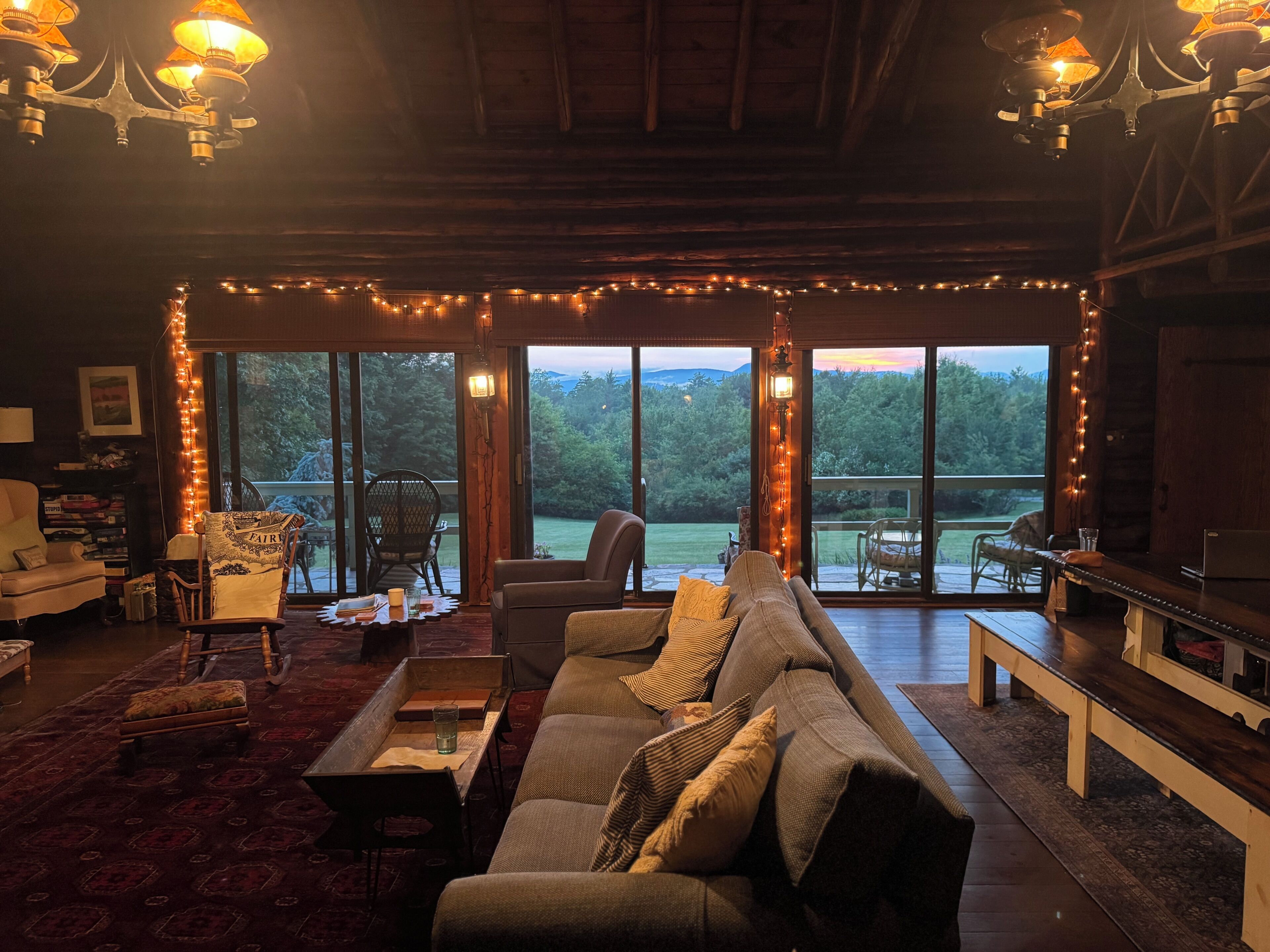 Una sala de estar acogedora con sofá, sillones y una mesa de centro. Amplias ventanas ofrecen vistas al exterior.