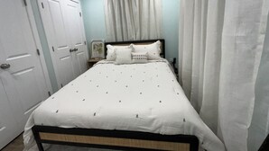 Un lit bien fait, avec un couvre-lit blanc et des oreillers, une tête de lit en bois et des rideaux blancs.