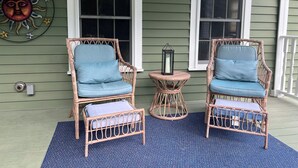 Two wicker chairs with blue cushions on a blue speckled floor, positioned on a porch with green siding and white trim.