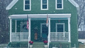 A green house with a white porch and two flags.
