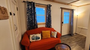 A cozy room with a red sofa, patterned curtains, a wooden door, and a floor lamp. - The Seneca Sunsets Studio (Burdett)